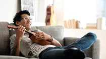 Content with his condo discount, a man reclines in his chair while strumming a ukulele.